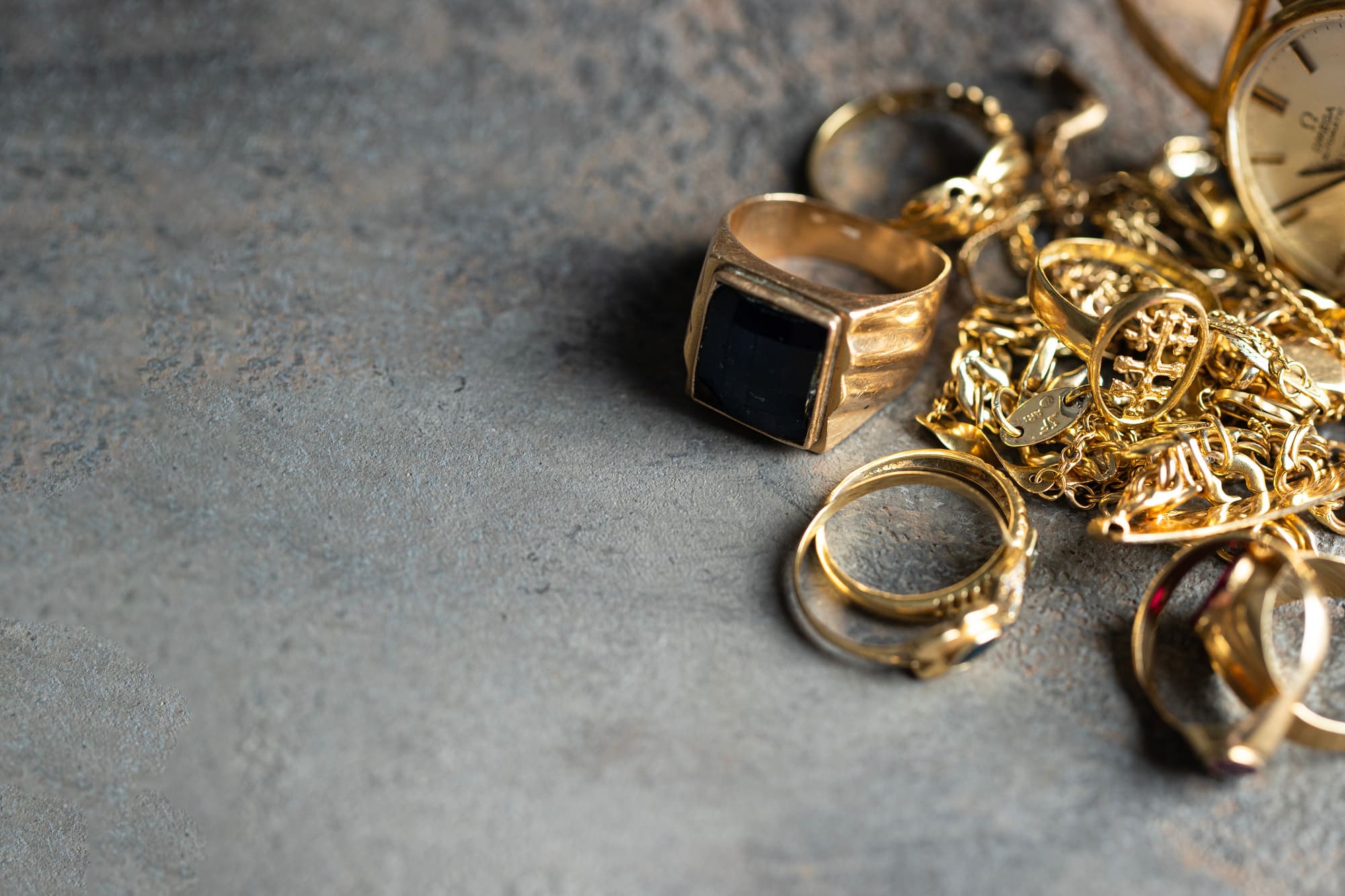 Bijoux en or, bagues, chaînes et montre ancienne déposés sur une surface grise.
